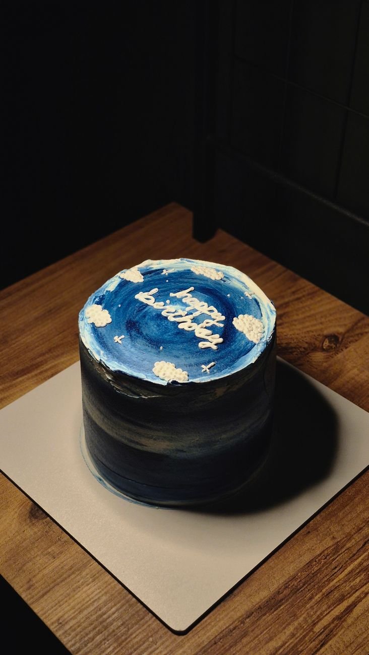 A sky-themed custom birthday cake on a wooden table in warm lighting