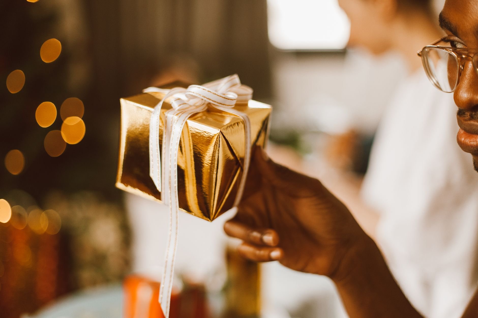 A beautifully packaged gift box with white ribbon, held with care